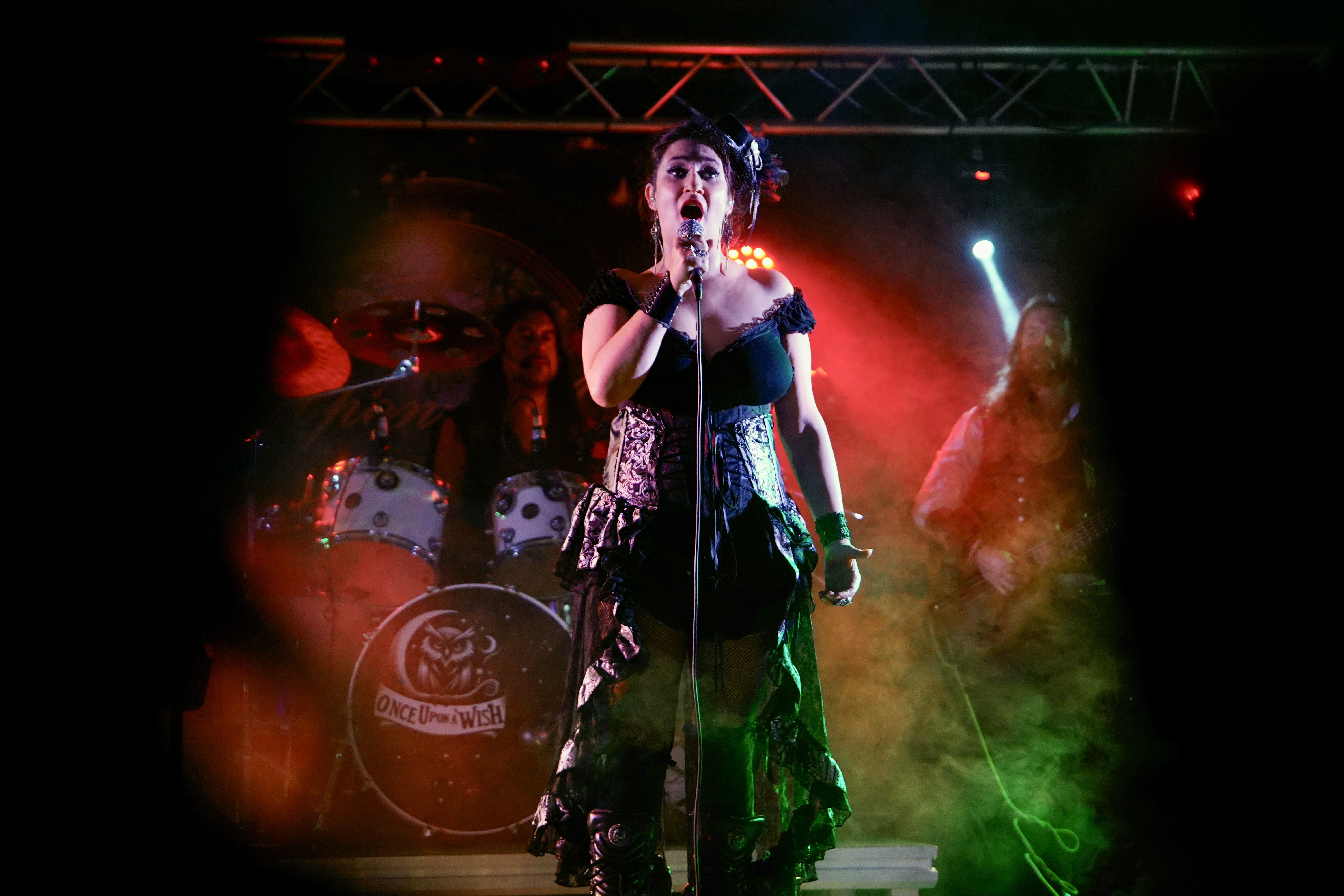 The image depicts a woman singing into a microphone on stage, with a band playing behind her. The woman is dressed in a bl...